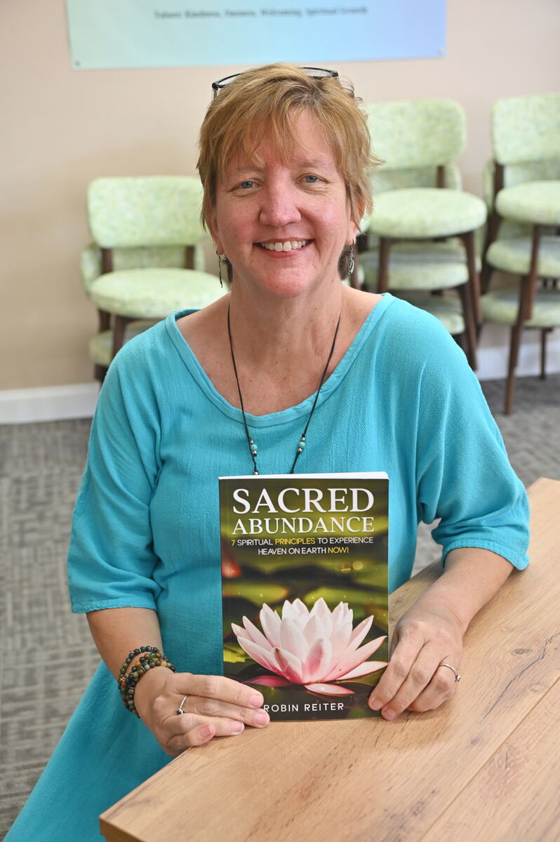 Rev. Robin Reiter seated at a table holding a copy of Sacred Abundance