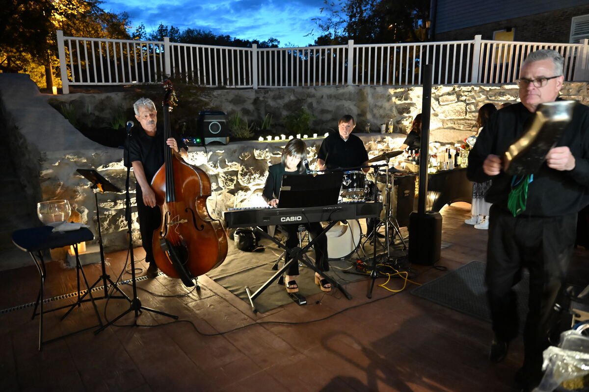 The band playing after dark on the lit patio, upright bass and keyboard, with guests standing nearby